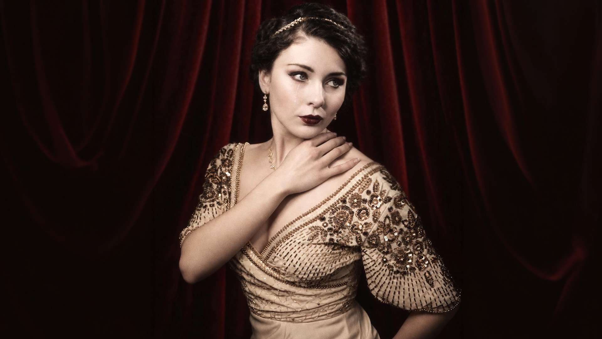 Megan Tremethick in a beaded vintage gown before red velvet curtains.